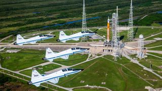 Four NASA T-38 training jets fly past the SLS rocket on the launch pad.