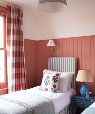 bedroom with red-pink panelled walls, single bed with blue and white striped headboard, red checkered curtains and cozy decor