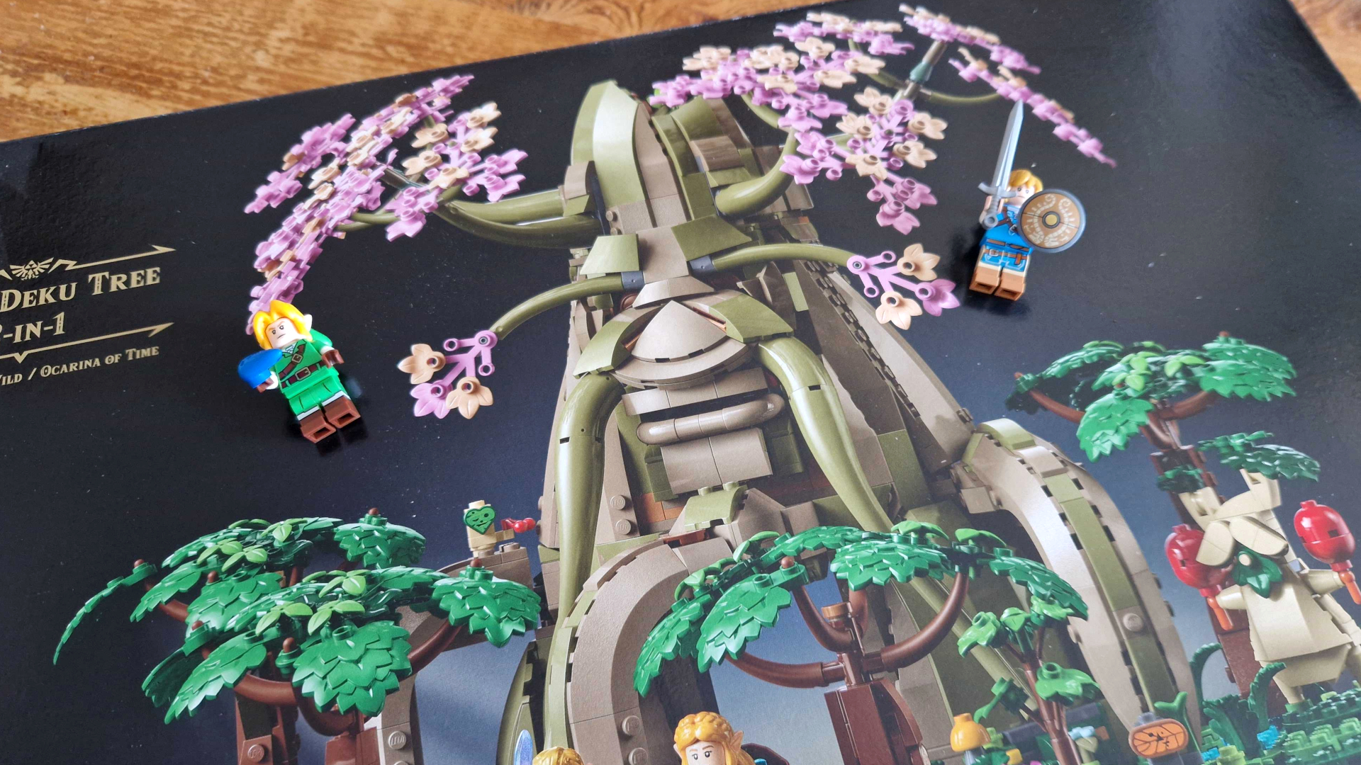 Lego The Great Deku Tree box on a wooden table, with two Link minifigures on top of it