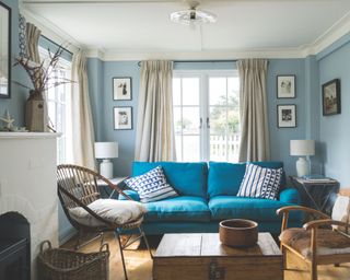 living room with pale blue walls, a bright blue sofa, a rattan chair and a chest as a coffee table