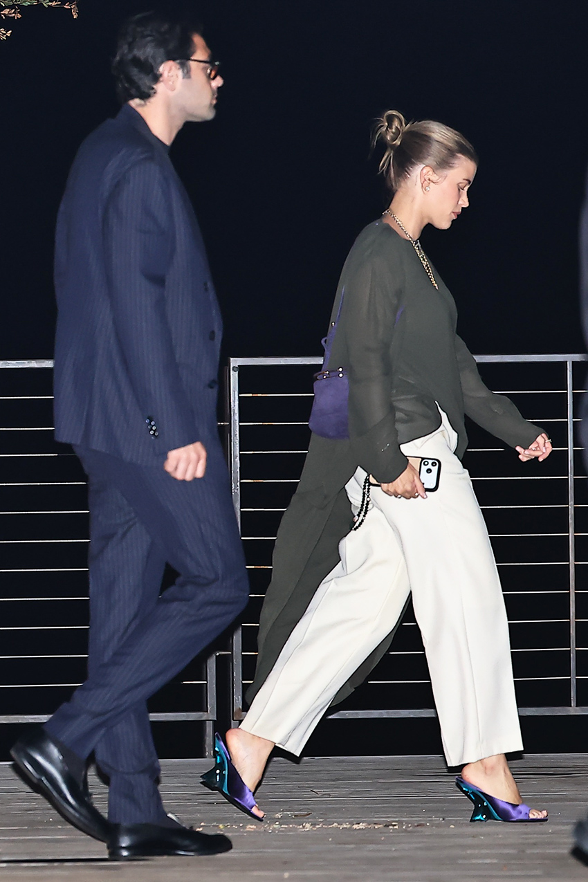 Sofia Richie and Elliot Grainge at Nobu Malibu, and she's wearing an asymmetrical long-sleeve gray top with wide-leg white pants and purple satin Dries Van Noten wedge mules
