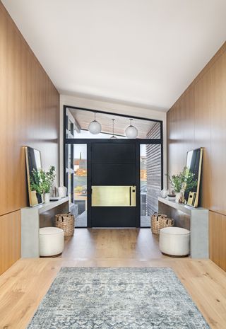 entryway with wood paneling and floor, rug, matching consoles, mirrors and footstools, black front door, vaulted ceiling