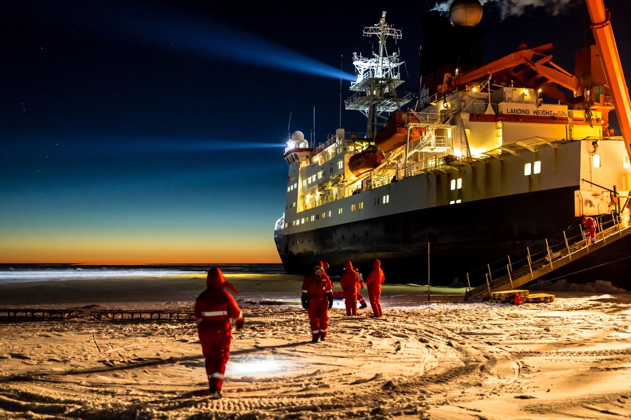 the RV polarstern icebreaker ship at night, surrounded by ice with lights hitting it