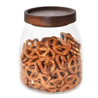 A glass storage jar with a wooden lid filled with pretzels, on a white background