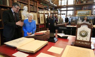 Queen Elizabeth II is shown items from the George III Collection pertaining to science and the Arts, including the 1765 Eardley Norton clock (R) by Royal Librarian Oliver Urquhart Irvine (L) while attending the launch of the George III Project at an event held in the Royal Library in Windsor Castle on April 1, 2015 in Windsor, England.