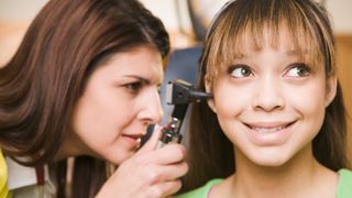 Female doctor examining teenage girl's ears using an otoscope