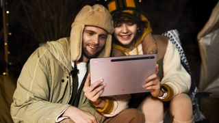 Samsung Galaxy Tab S8 Android tablet being used by two young people, one a man, the other a woman, sat down at night outdoors