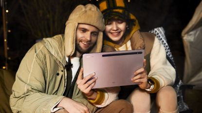Samsung Galaxy Tab tablet being used by two young people, one a man, the other a woman, sat down at night outdoors