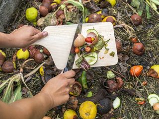 Hands scraping food scraps from a cutting board into a compost heap