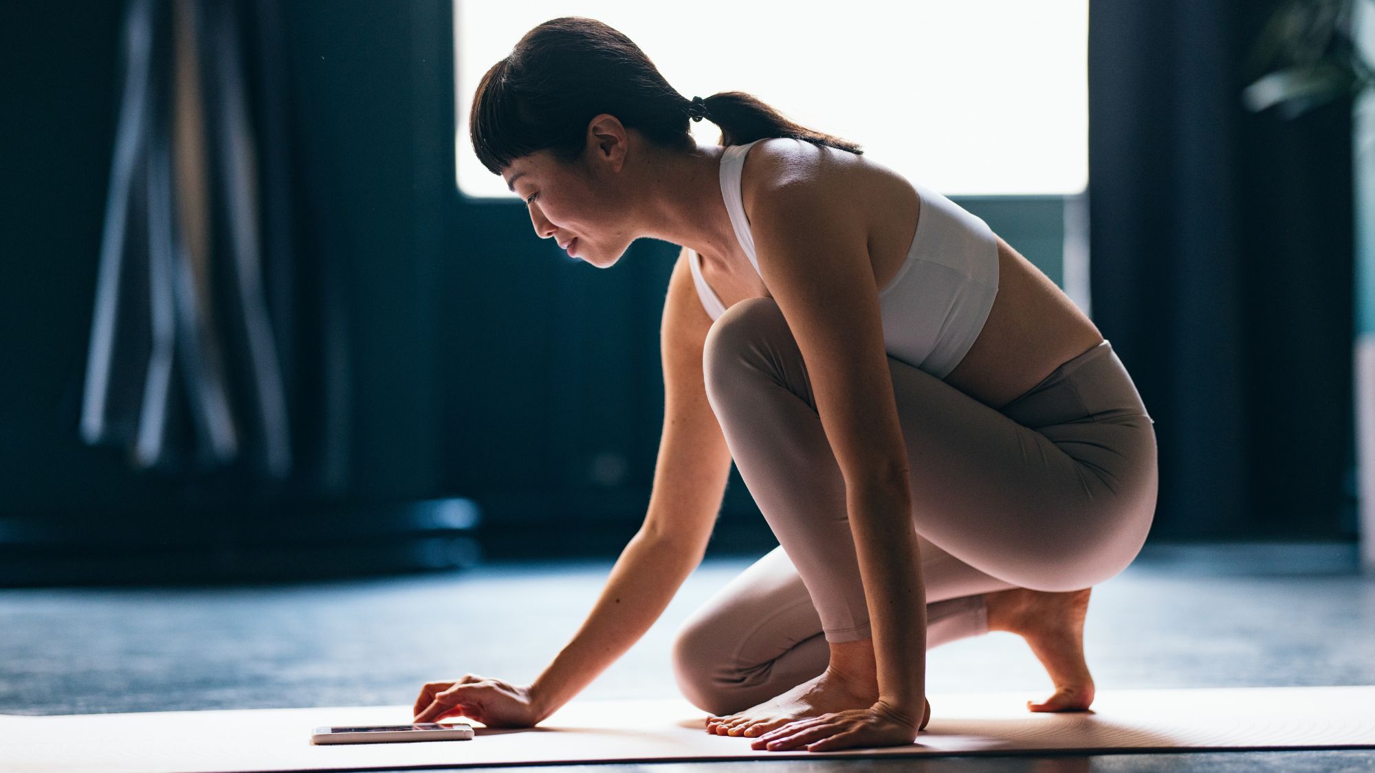 A woman in pink and white gym gear on a yoga mat, ready to do a Pilates workout