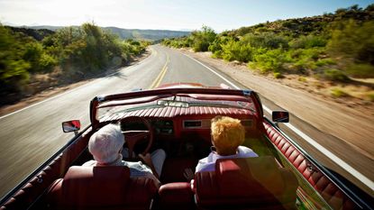 senior couple driving on road in a convertible