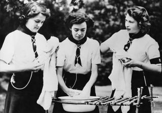 Princess Elizabeth (later Queen Elizabeth II, right), helps with the washing up at a Girl Guides camp at Windsor, Berkshire, 25th July 1944. The princess is Patrol Leader of the Buckingham Palace company of guides