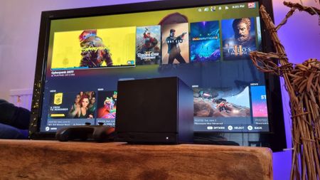 A Steam Machine in front of a TV, showing the SteamOS interface running in the background