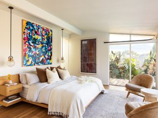 master bedroom in neutral colors with colorful artwork above bed