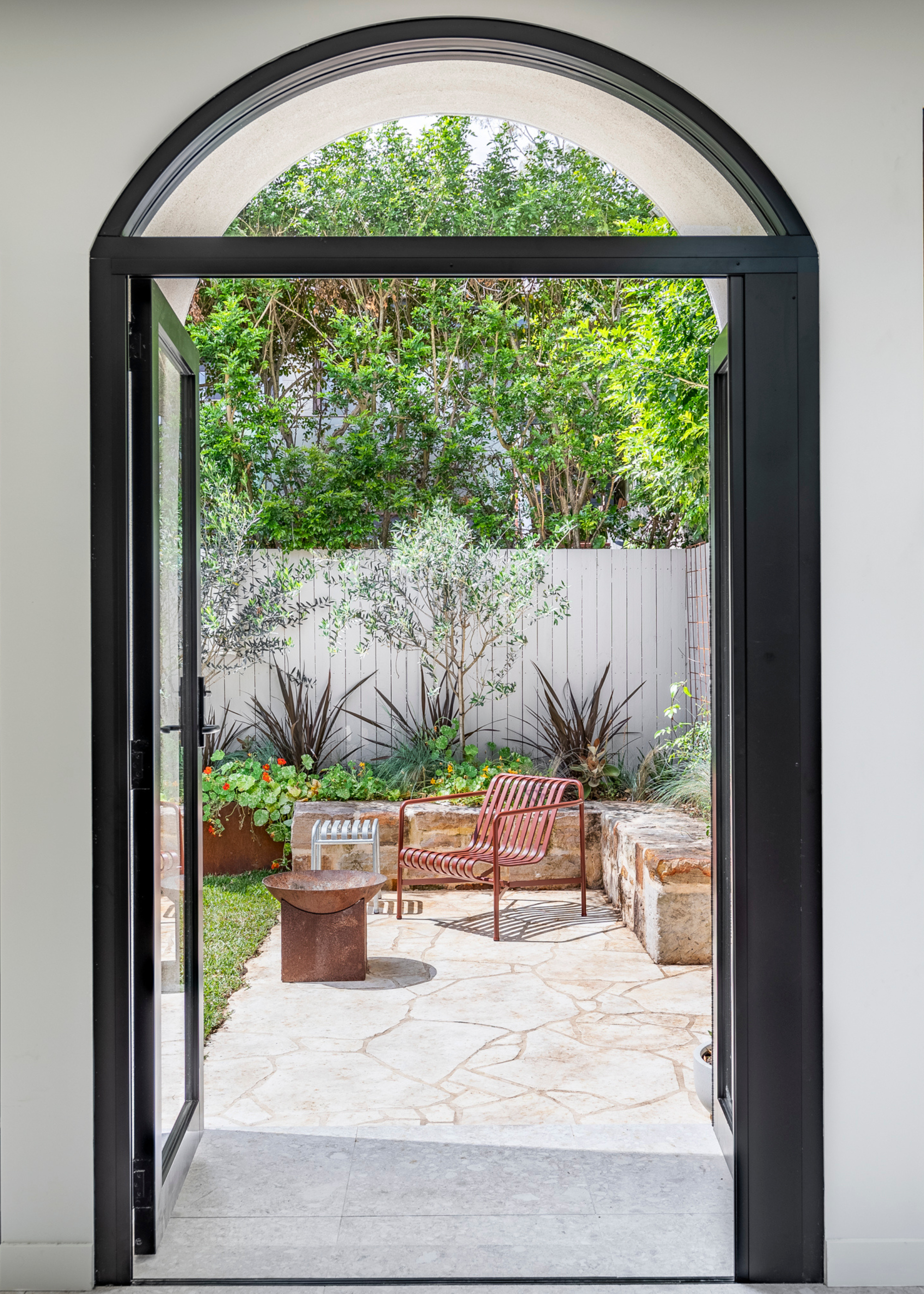 An arched doorway leading to a patio with metal furniture, a wall of trough planters and a side table