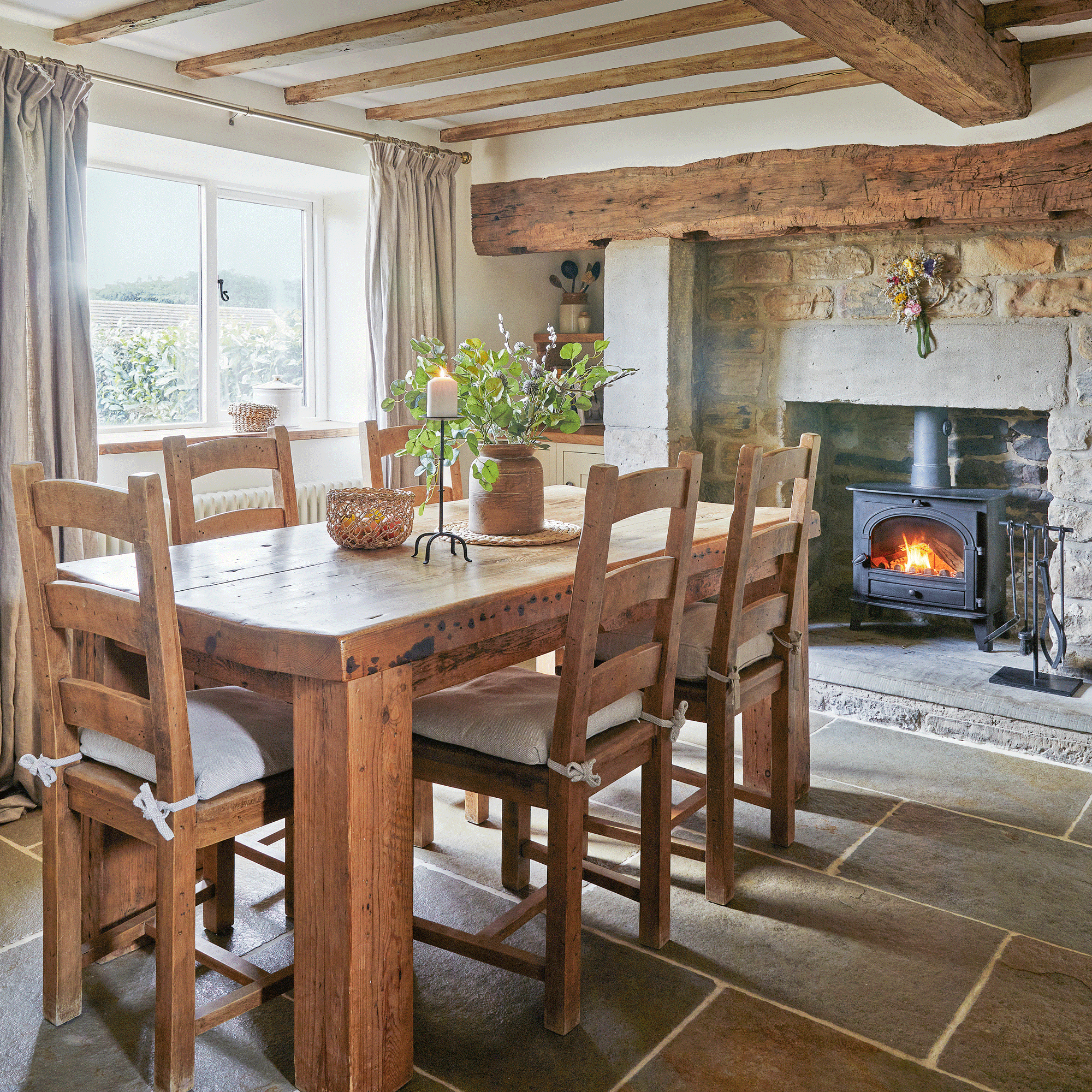a dining room with large format stone flooring an wooden dining table and chairs and a large fireplace with a woodburner