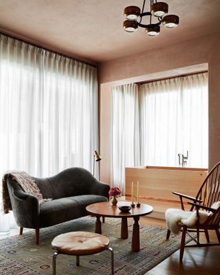 Taupe room with a wooden bathtub, dark gray love seat, a wooden accent table, and a wooden chair with a fuzzy throw blanket