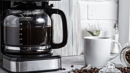 A drip coffee maker on a kitchen counter beside a full coffee cup