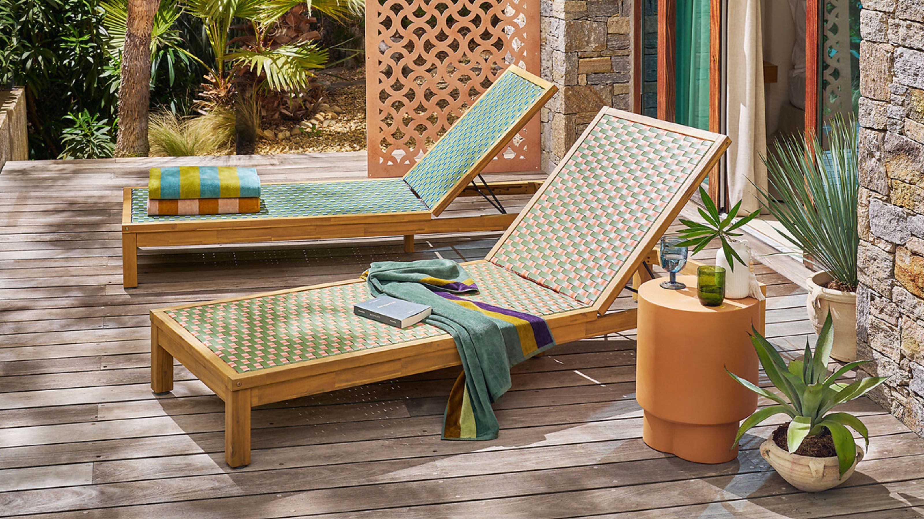 La Redoute sun loungers with colorful woven rattan-like finish with potted plants, and colorful towels on a deck