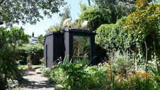 A garden room in a garden with lots of plants and trees surrounding it. In this garden room, the Shou Sugi Ban technique has been used.