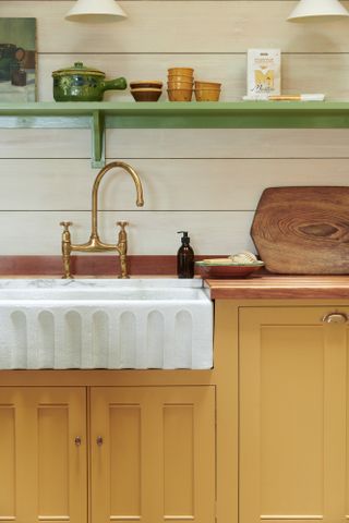 Yellow base cabinet and marble textured sink with brass tap, green wooden shelf