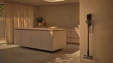 Dyson V8 Cyclone mounted on wall in muted beige kitchen area with curtains and kitchen island.