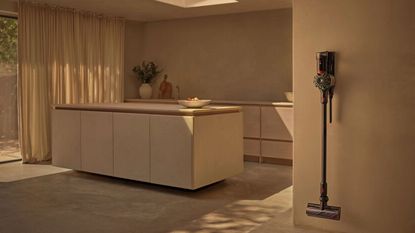 Dyson V8 Cyclone mounted on wall in muted beige kitchen area with curtains and kitchen island.