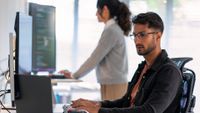 Cybersecurity workers sitting and standing in an office space while working on laptop devices.