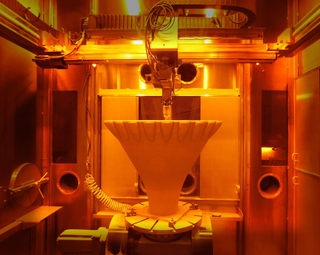 a cone-shaped rocket nozzle inside a massive 3D printer