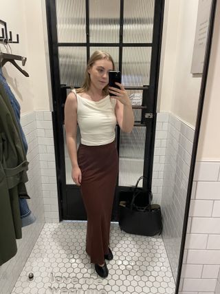 Woman in dressing room wears white twist top, brown linen skirt, black ballet flats