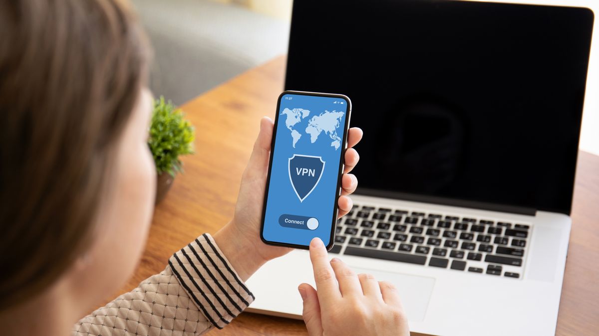 Woman using a free VPN on a mobile device, in front of a laptop