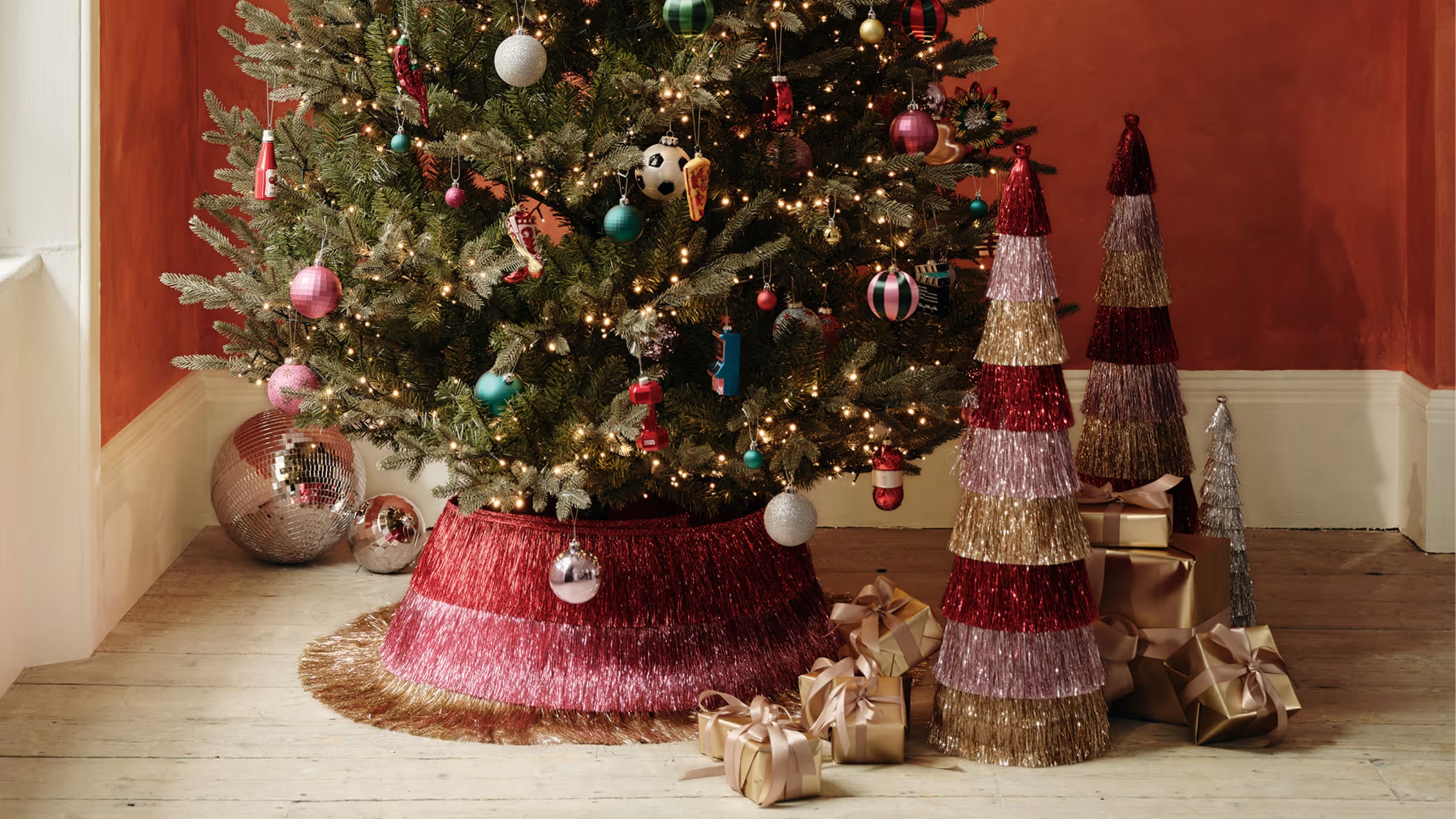 a christmas tree with a tinsel tree skirt and small colorful tinsel trees next to it with small gold presents and disco balls