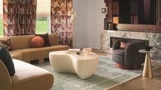 a living room in a warm color scheme with patterned curyains, a patterned rug and a marble fireplace with a tv mounted above