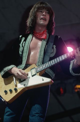 Guitarist Rick Derringer on stage performing. He is shown in a 3/4-length view, wearing a bolero jacket. Photograph, 1976.