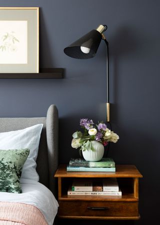 An example of black bedroom ideas showing a close up shot of a bedside table in front of a black wall