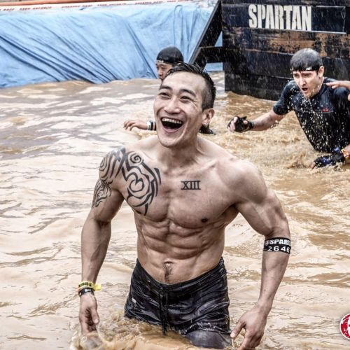 man featured in water from hips up topless looking toward the camera smiling.