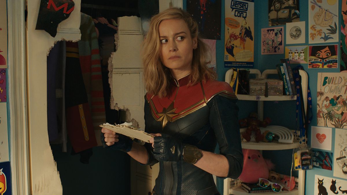 Captain Marvel looks puzzled as she stands in Kamala Khan&#039;s room in The Marvels