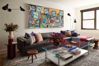 a living rom with colorful artwork, a leather sofa and glass coffee table