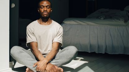 Man sat on the floor of a bedroom meditating