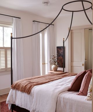 neutral bedroom with a black iron four posted bed and warm terracotta pink accents