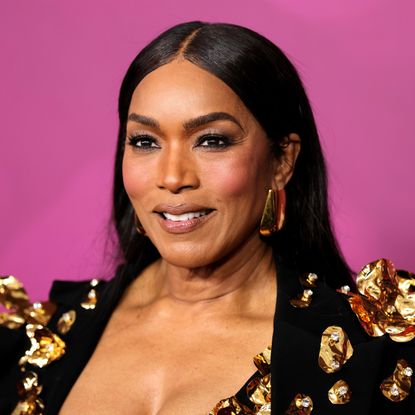 a black woman with dark hair poses in front of a pink background