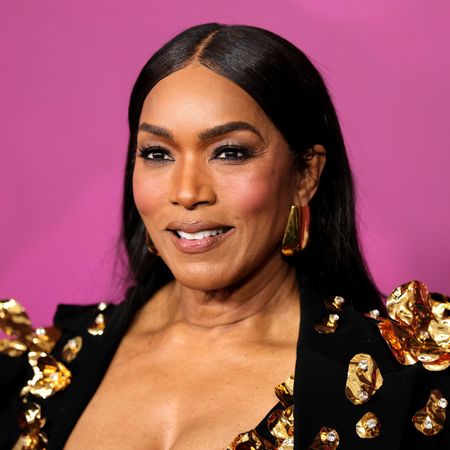 a black woman with dark hair poses in front of a pink background