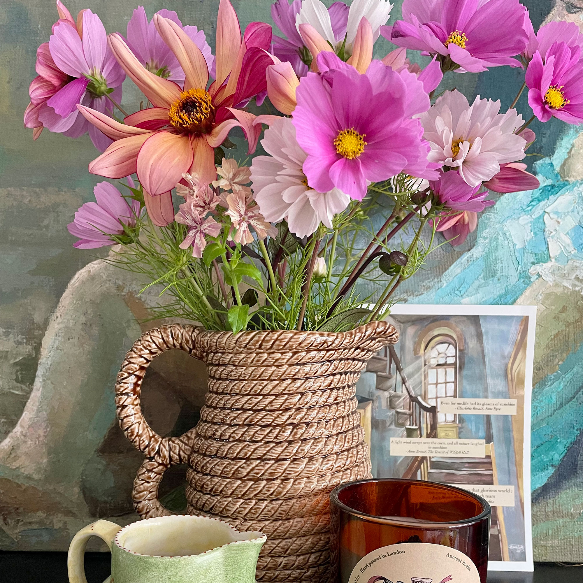 Ceramic jug filled with pink flowers in front of painting