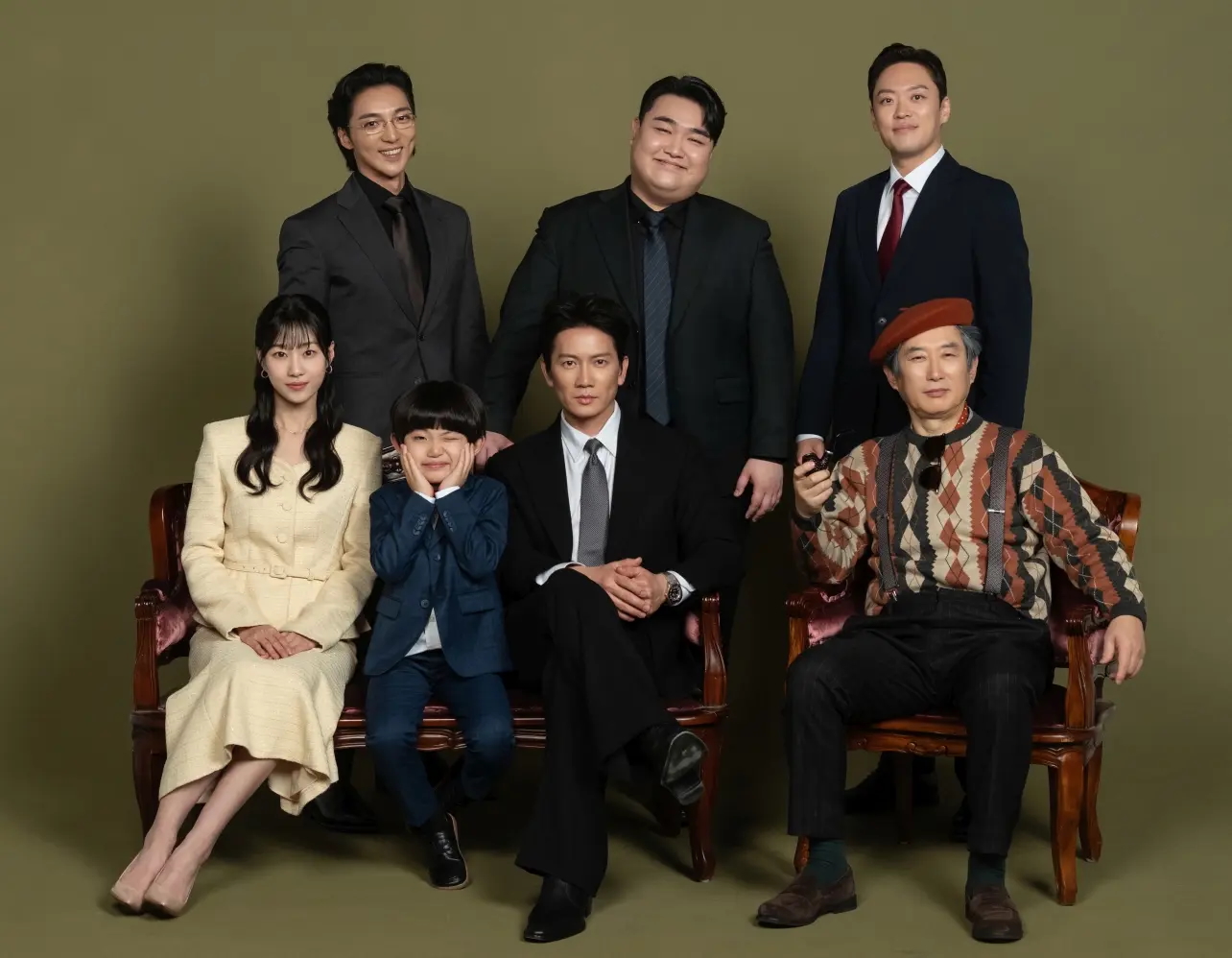 a portrait of a korean family featuring three men in suits, a woman in a yellow skirt suit, a young boy, a man in a suit, and an older man in an argyle sweater and beret for 'The Apartment Job.'