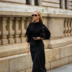 woman wears all black skirt outfit with black accessories and boots while walking
