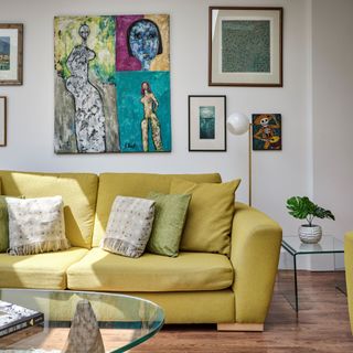 Green sofa with cushions, hanging artwork, glass side and coffee table in white painted living room