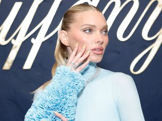 Elsa Hosk looked away from the camera with her hand on her face in her blue dress