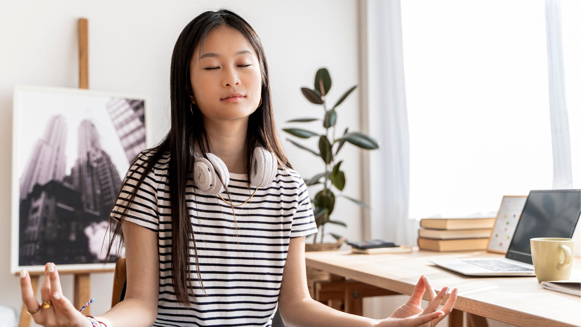 A female student meditates with her eyes closed as she sits near her desk.