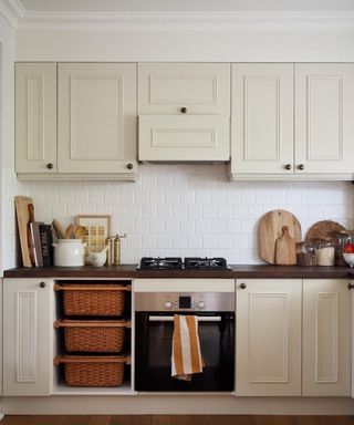 Taupe kitchen cabinets with distressed brass hardware and dark wood countertops.