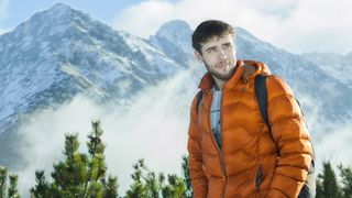 wash a down jacket: hiker wearing down jacket with mountain backdrop